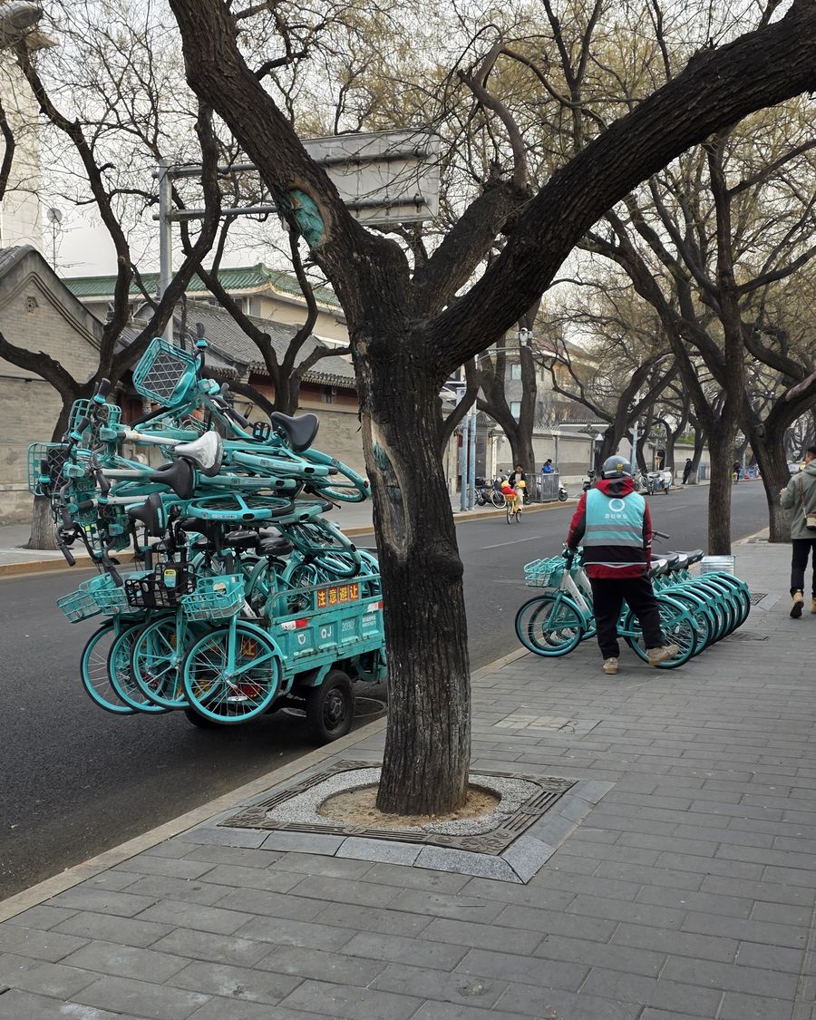 A worker next to a small vehicle stacked high with shared bikes on a street in Beijing