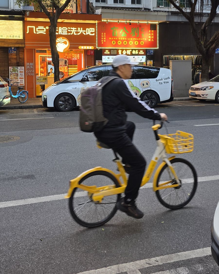 A man riding a yellow shared bike across a street in Guangzhou